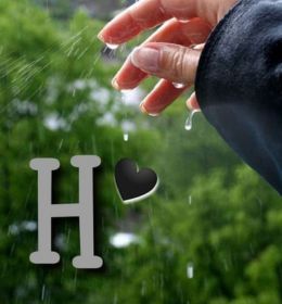 A hand reaching out in the rain with water droplets falling. The letter "H" with a black heart symbol is overlaid on the image.