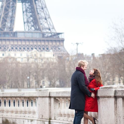 A couple sitting on a picnic blanket by a river, holding hands and enjoying nature.