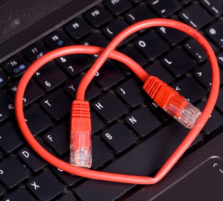 A red Ethernet cable shaped into a heart lies on a black laptop keyboard, symbolizing digital love and connection.
