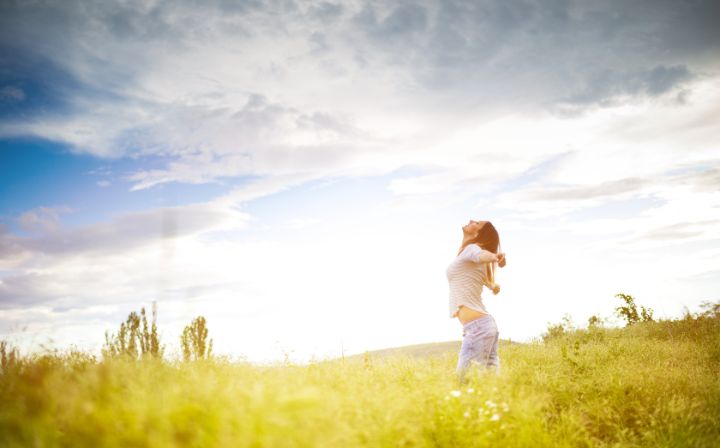 A young woman standing in a field with her arms stretched, enjoying the fresh air under a cloudy sky.