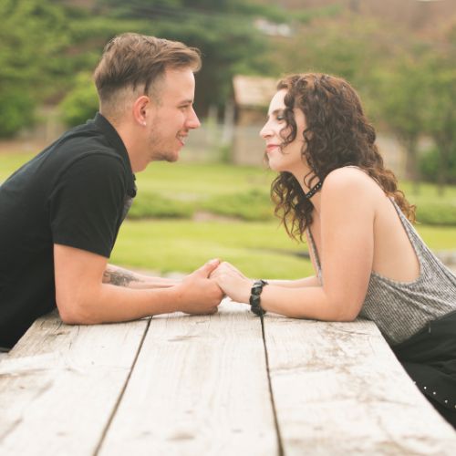 A couple sitting together at a wooden table in a park