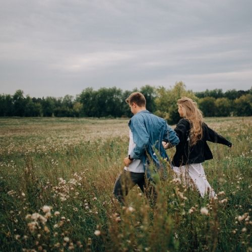 A couple strolls hand in hand through a vibrant field filled with colorful wildflowers under a clear blue sky