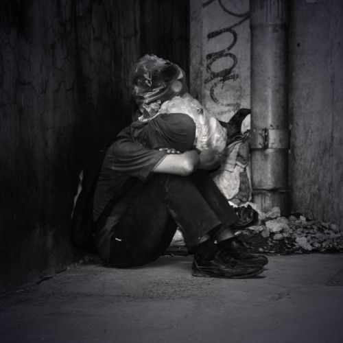 A homeless man sits on the ground, head in hands, conveying a sense of despair and hopelessness
