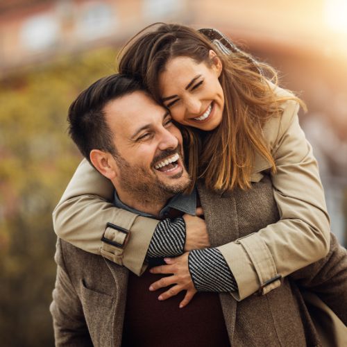 A man and woman embrace, laughing and smiling joyfully together in a warm, affectionate moment