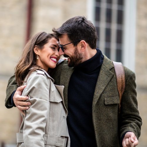 A man and woman embrace warmly in a bustling street, surrounded by city life