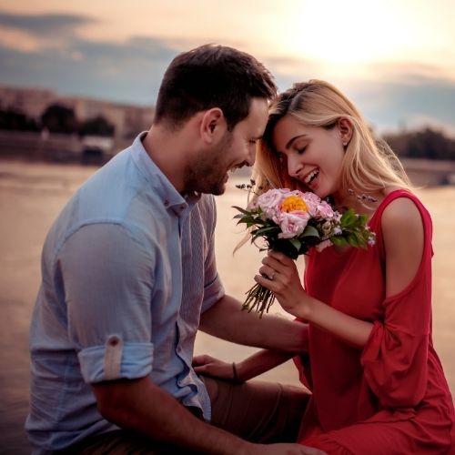 A man and woman sit on the ground each holding a bouquet of colorful flowers