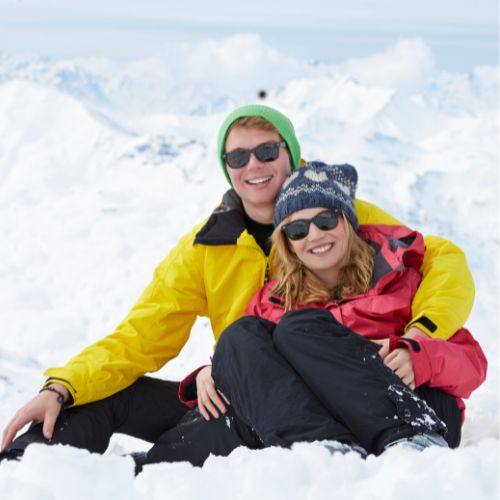 A man and woman sitting together on a snowy landscape, enjoying the winter scenery