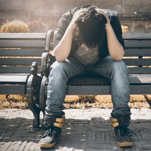 A man sits on a bench resting his head in his hands