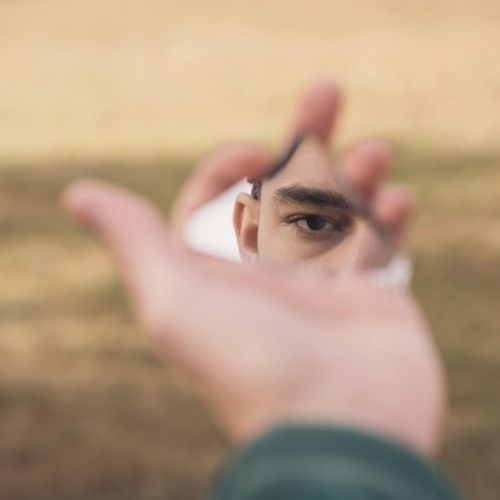 A person holds a mirror up to their face, reflecting their features and expression