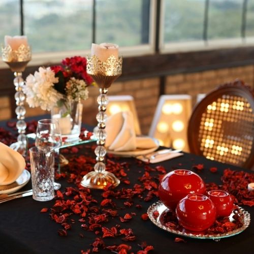A table elegantly set with red and black decorations, featuring plates, cutlery, and a centerpiece