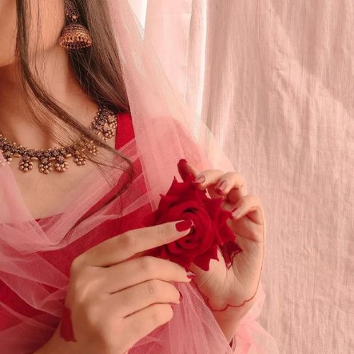 A woman in a red dress gracefully holds a single rose, exuding elegance and charm