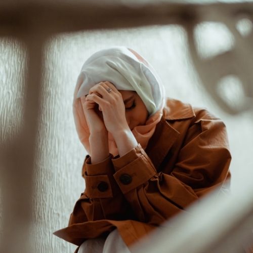 A woman wearing a brown coat and headscarf sits on a stairway