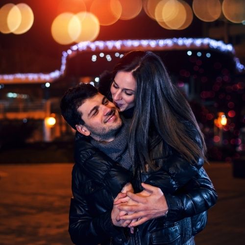 A young couple embraces joyfully in front of a beautifully decorated Christmas tree