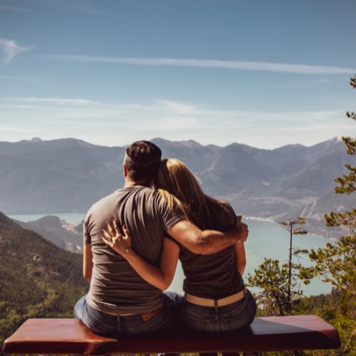 Couple sitting on a bench, enjoying a scenic view of a lake and mountains in the background