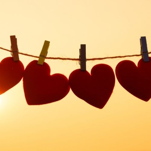 Four red hearts are clipped to clothes pegs, with a bright sun shining in the background