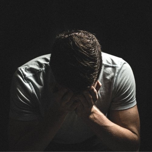 Man sitting in a dark room with his hands covering his face, conveying a sense of distress or contemplation