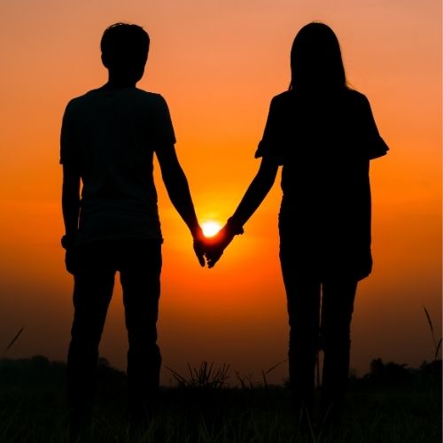 Silhouette of a couple holding hands against a vibrant sunset backdrop