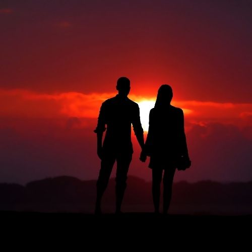 Silhouette of a couple holding hands against a vibrant sunset backdrop