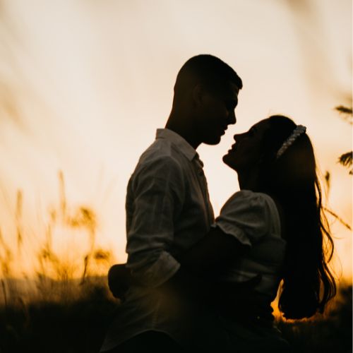 Silhouette of a couple standing in a field during a vibrant sunset, with warm colors illuminating the sky