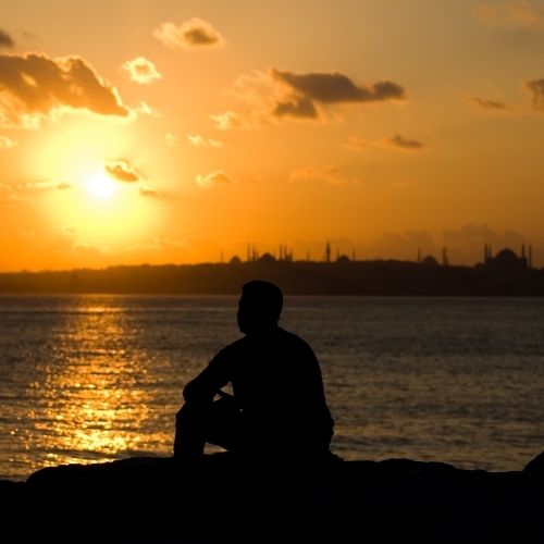Silhouette of a man sitting on a rock at sunset, with a city skyline visible in the background
