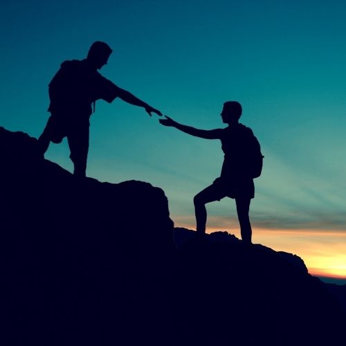 Two people reaching out to each other while standing on top of a mountain