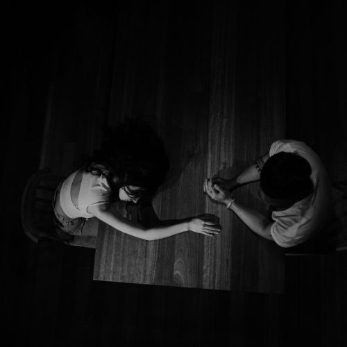 Two people seated at a table surrounded by darkness creating an intimate and mysterious atmosphere