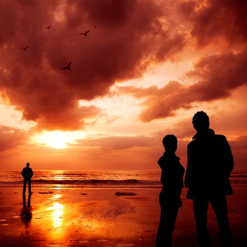 Two people stand on the beach, silhouetted against a vibrant sunset sky