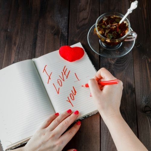 Woman writing in a notebook with a red heart drawn on the page