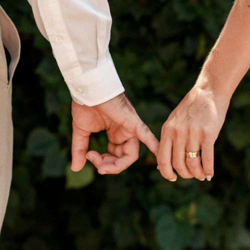 A couple holding hands, positioned in front of a vibrant bush, symbolizing connection and togetherness