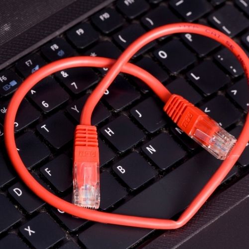 A red Ethernet cable plugged into a laptop keyboard, indicating a wired internet connection