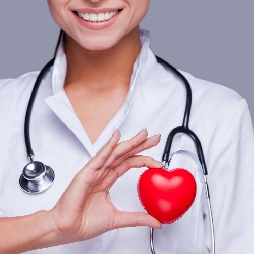 A woman in a white coat holds a red heart, symbolizing care and compassion in a medical or supportive context