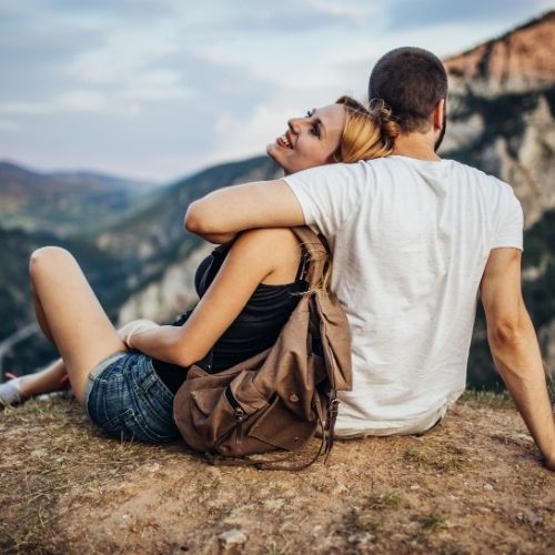 Couple sitting on a mountain peak, facing away from the camera, enjoying the scenic view together
