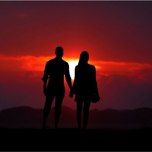 Silhouette of a couple holding hands against a vibrant sunset backdrop