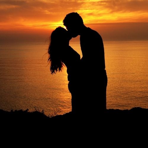 Silhouette of a couple kissing against a vibrant sunset backdrop, creating a romantic and intimate atmosphere
