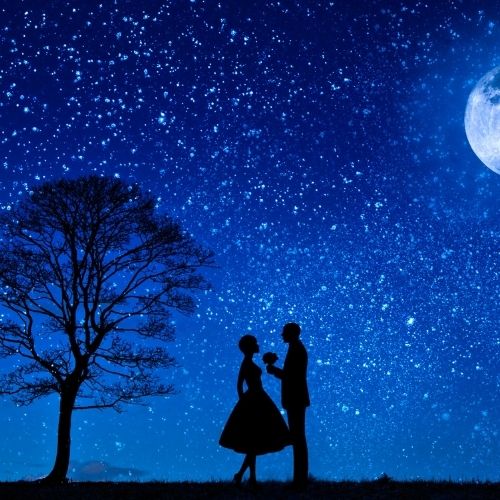 Silhouette of a couple standing together under a bright full moon against a dark night sky