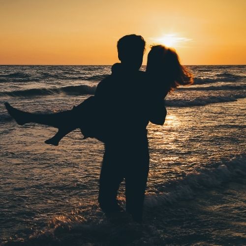 Silhouette of a man carrying a woman on his back against a vibrant sunset backdrop
