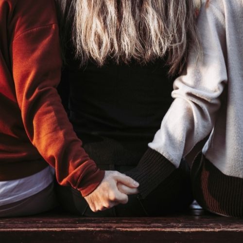 Three people sitting on a bench, holding hands and enjoying each other's company in a serene outdoor setting