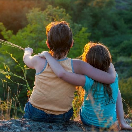 Two children sit on a rock, embracing each other with smiles