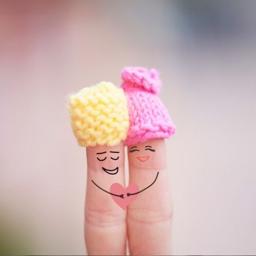 Two fingers wearing colorful knitted hats, playfully showcasing a whimsical and cozy accessory