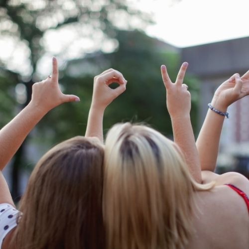 Two girls smiling and making the peace sign with their hands, conveying a message of friendship and positivity