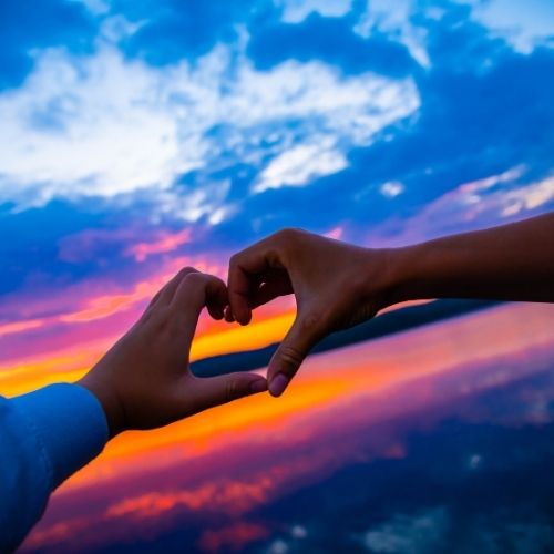 Two people create a heart shape with their hands above a serene lake