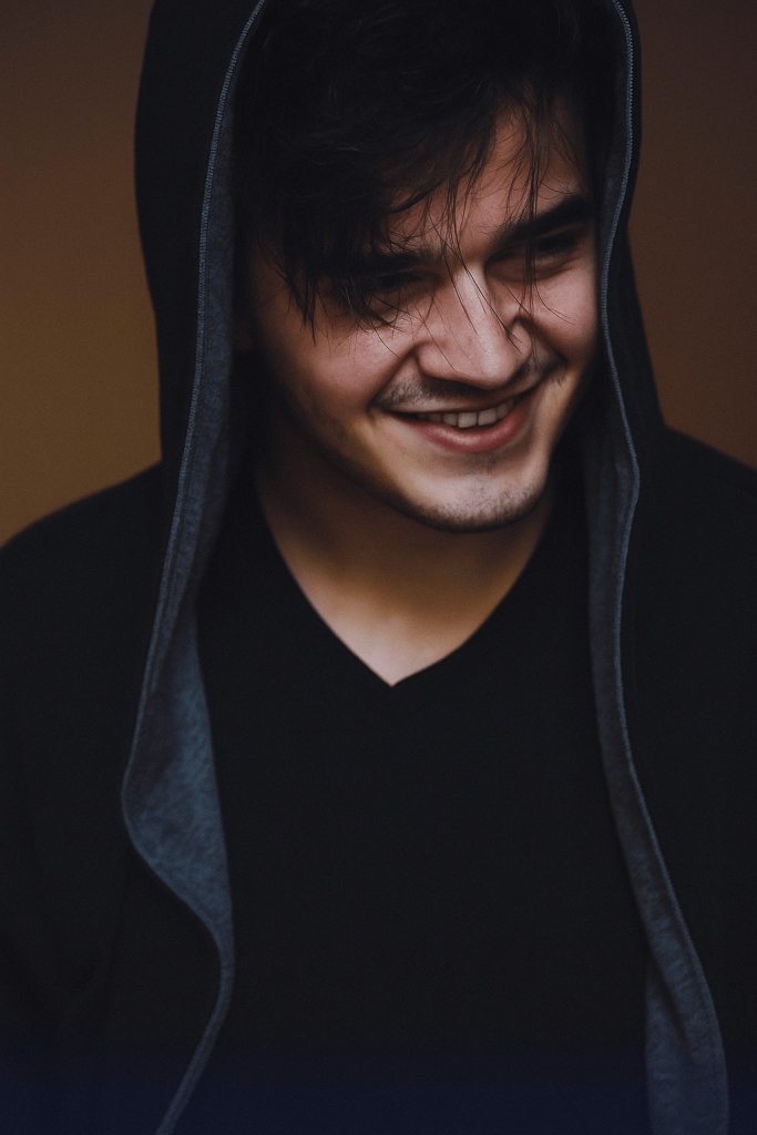 A man in a hoodie smiles warmly while looking directly at the camera