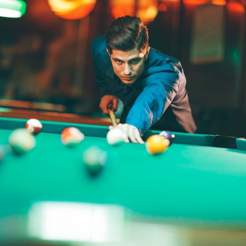 A man is focused on playing pool at a bar