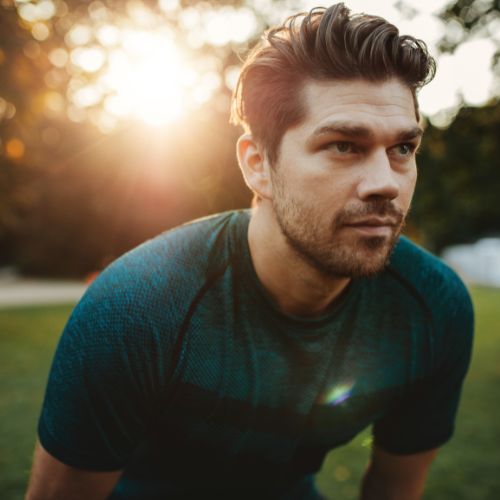 A man sitting on grass looks directly at the camera with a neutral expression