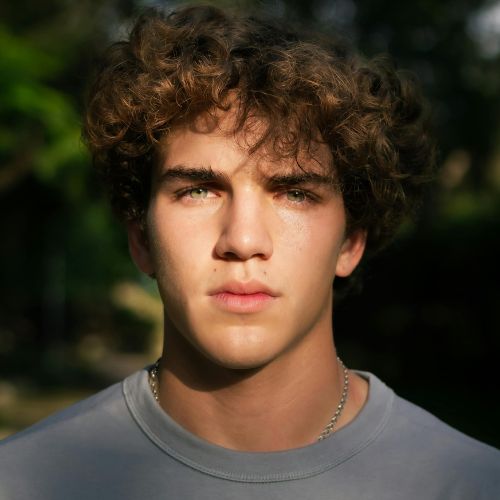 A young man with curly hair gazes directly at the camera