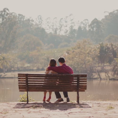A couple sits on a bench by a serene lake