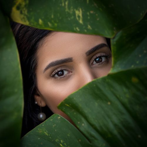 A woman peeks out from behind green leaves