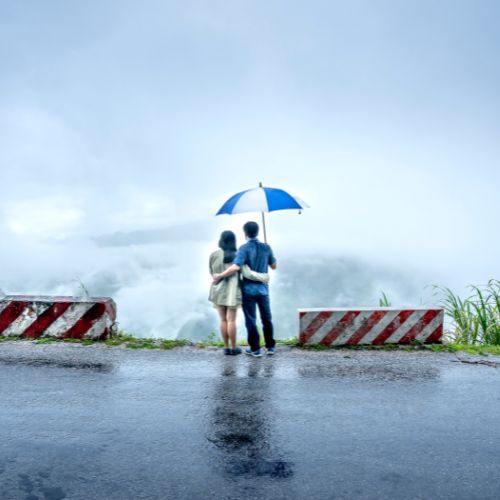 Couple standing under a colorful umbrella on a rainy road
