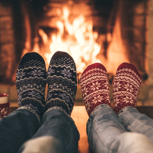 Two people in socks and mittens relax together in front of a cozy fireplace