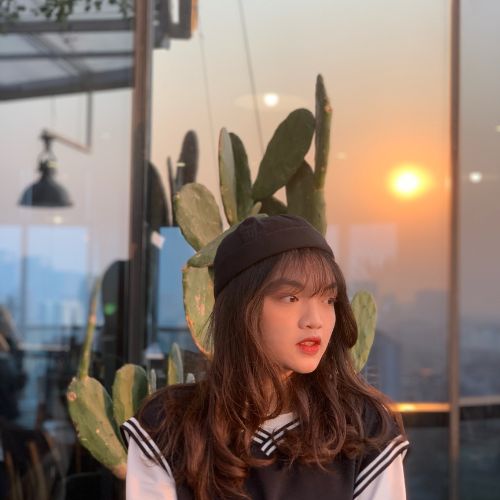 A girl in a black and white striped shirt and beanie sits in front of a cactus